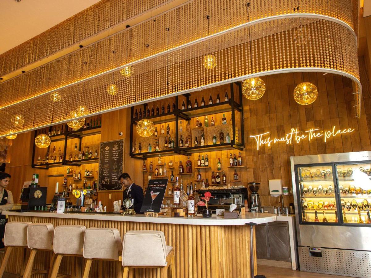 a bar with a man sitting at a counter at Novotel Hyderabad Airport in Hyderabad