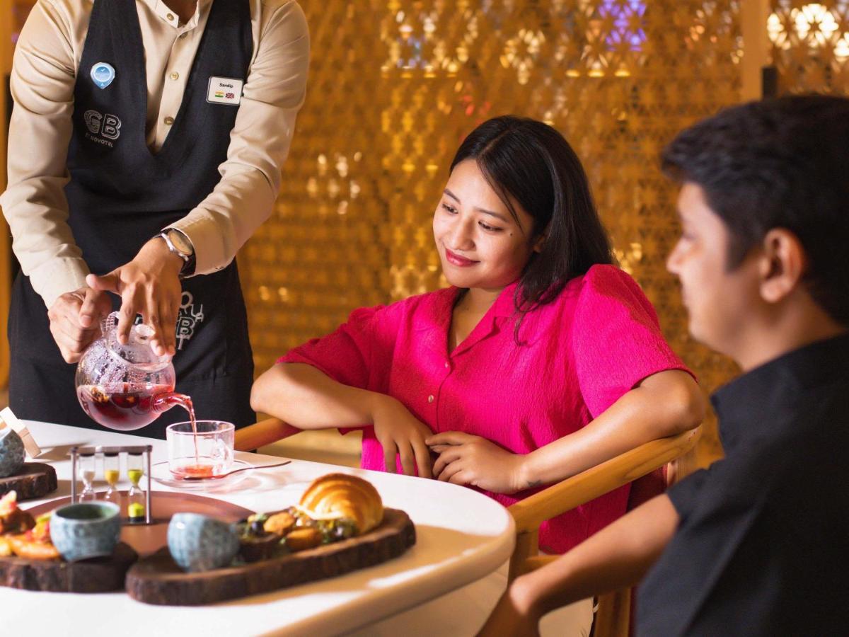a woman sitting at a table in a restaurant with a waiter at Novotel Hyderabad Airport in Hyderabad