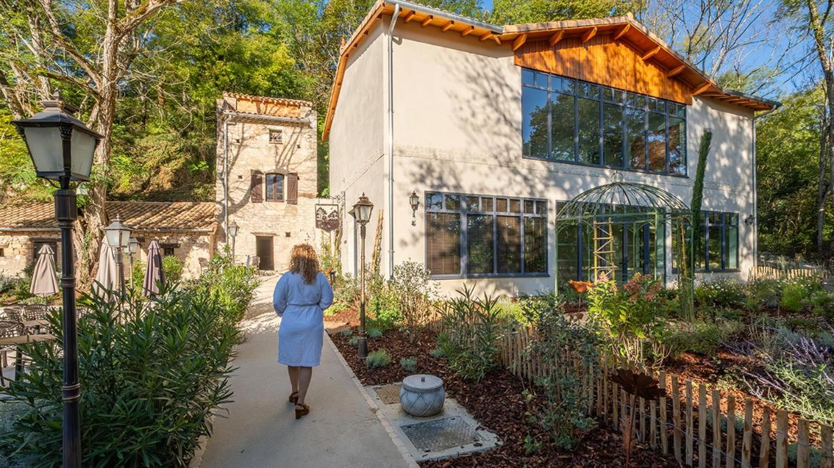 une femme marchant sur un trottoir devant une maison dans l'établissement Le Belvédère Hotel et Bien être, à Lauzerte