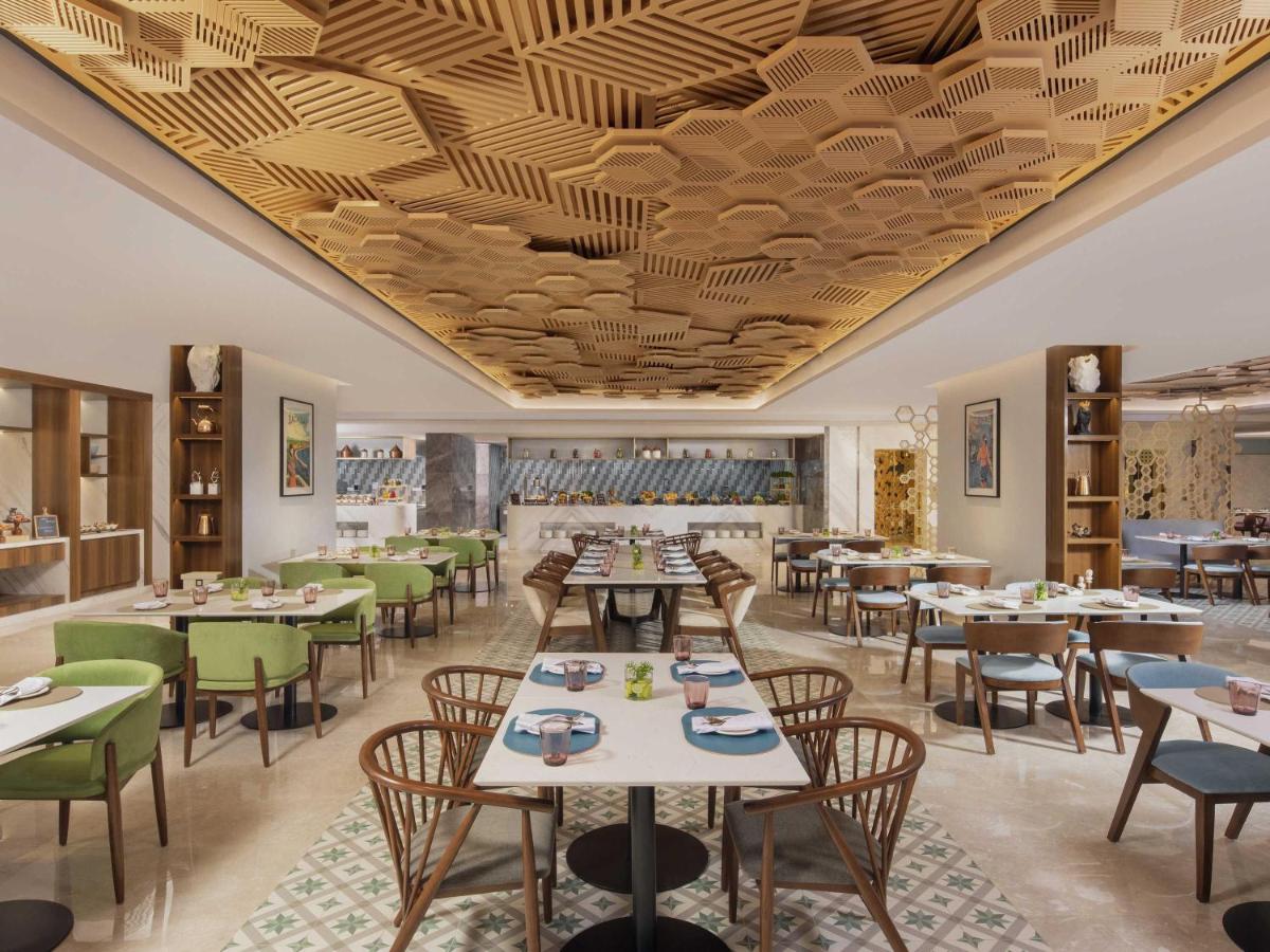a restaurant with tables and chairs and a wooden ceiling at Novotel Mumbai International Airport in Mumbai
