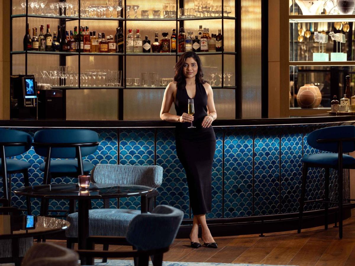 a woman standing at a bar holding a glass of wine at Pullman Chennai Anna Salai - Premium Brand By Accor in Chennai