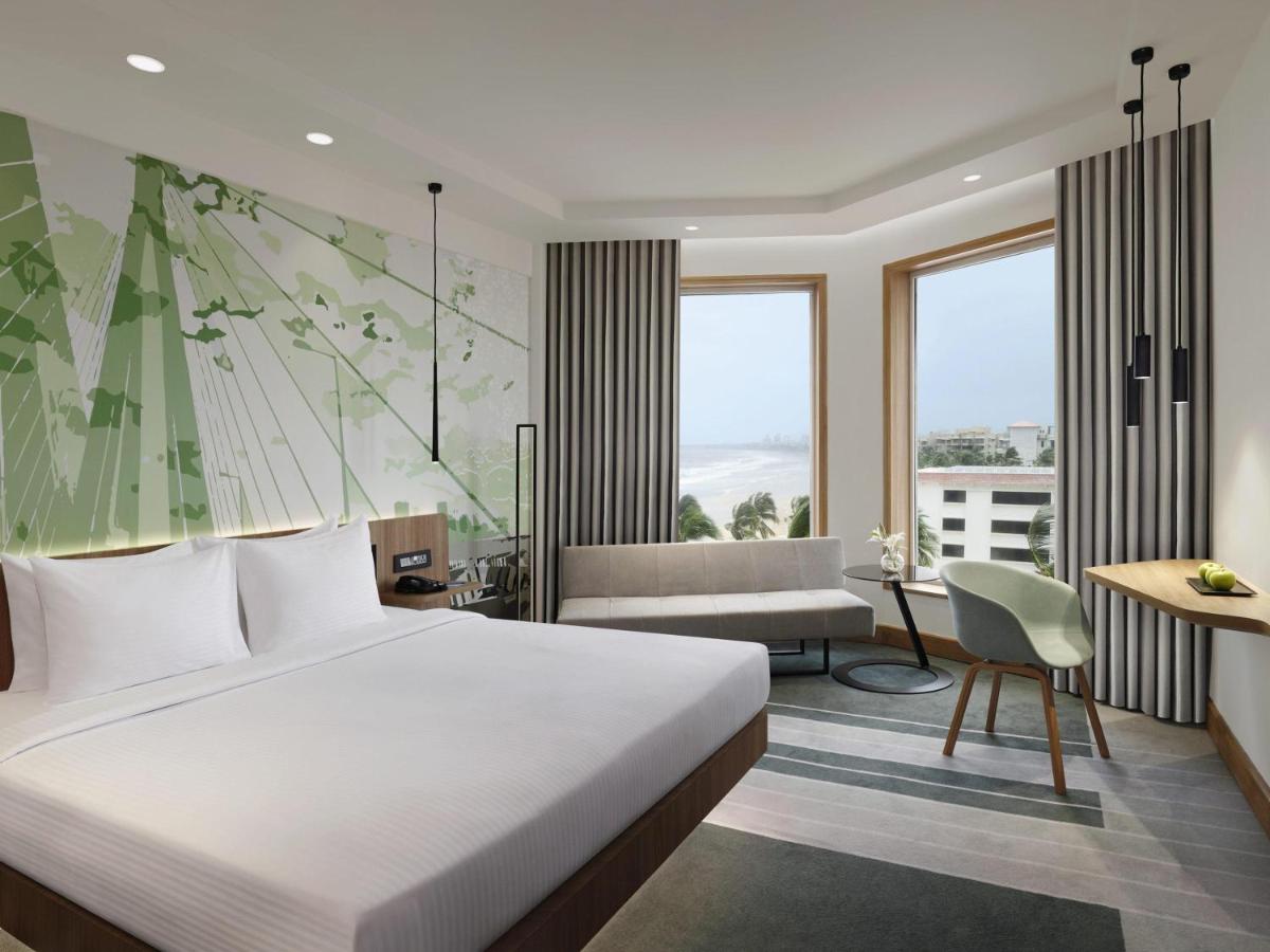 a hotel room with a bed and a couch and windows at Novotel Mumbai Juhu Beach in Mumbai