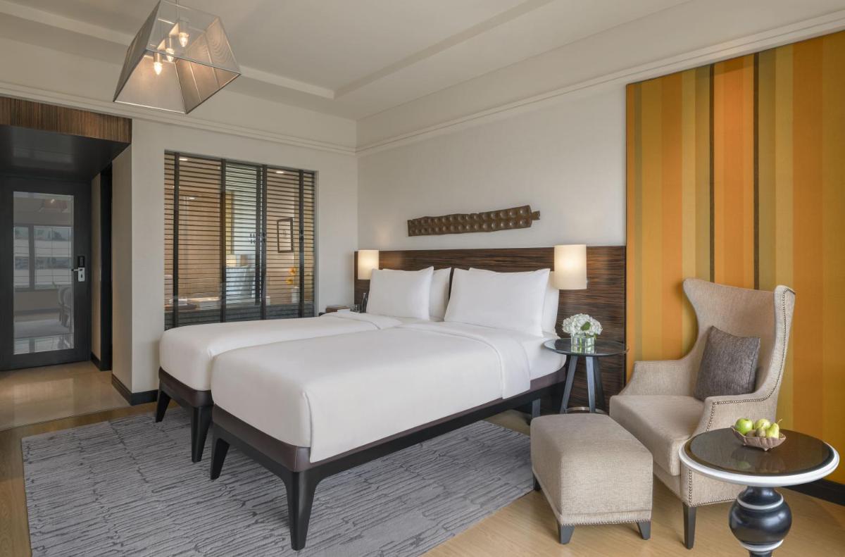 a bedroom with a large white bed and a chair at The Raintree, St. Mary’s Road in Chennai