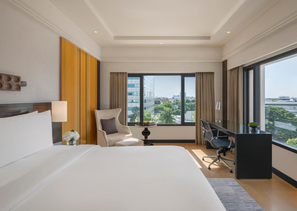 a hotel room with a bed and a desk and windows at The Raintree, St. Mary’s Road in Chennai