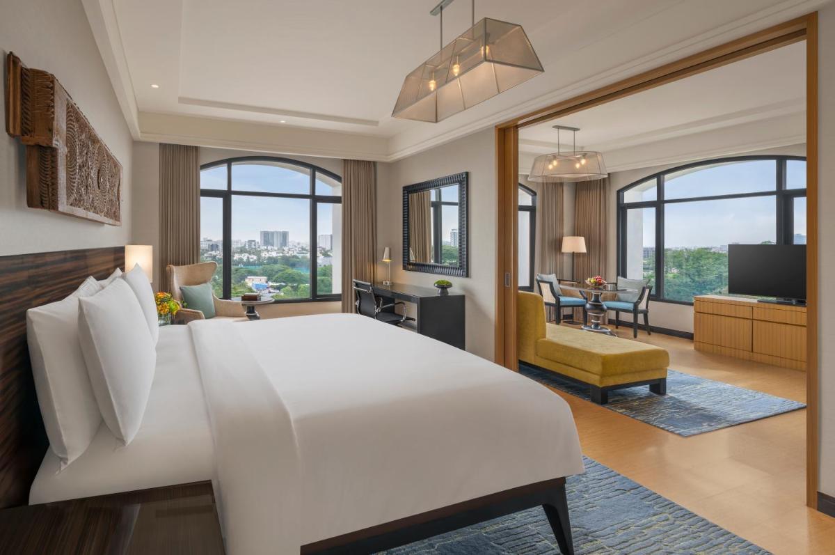 a bedroom with a large white bed and a living room at The Raintree, St. Mary’s Road in Chennai
