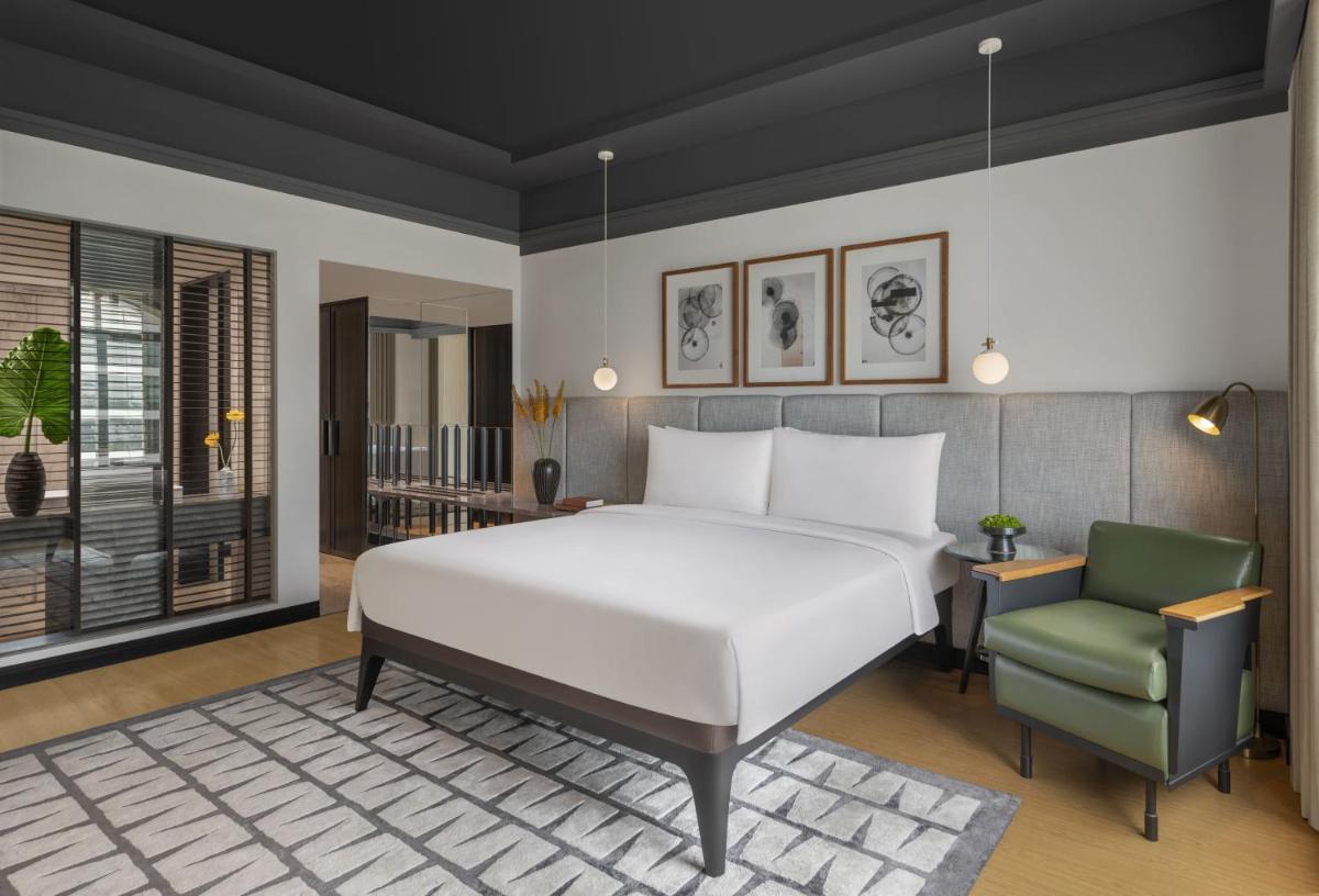 a bedroom with a white bed and a green chair at The Raintree, St. Mary’s Road in Chennai