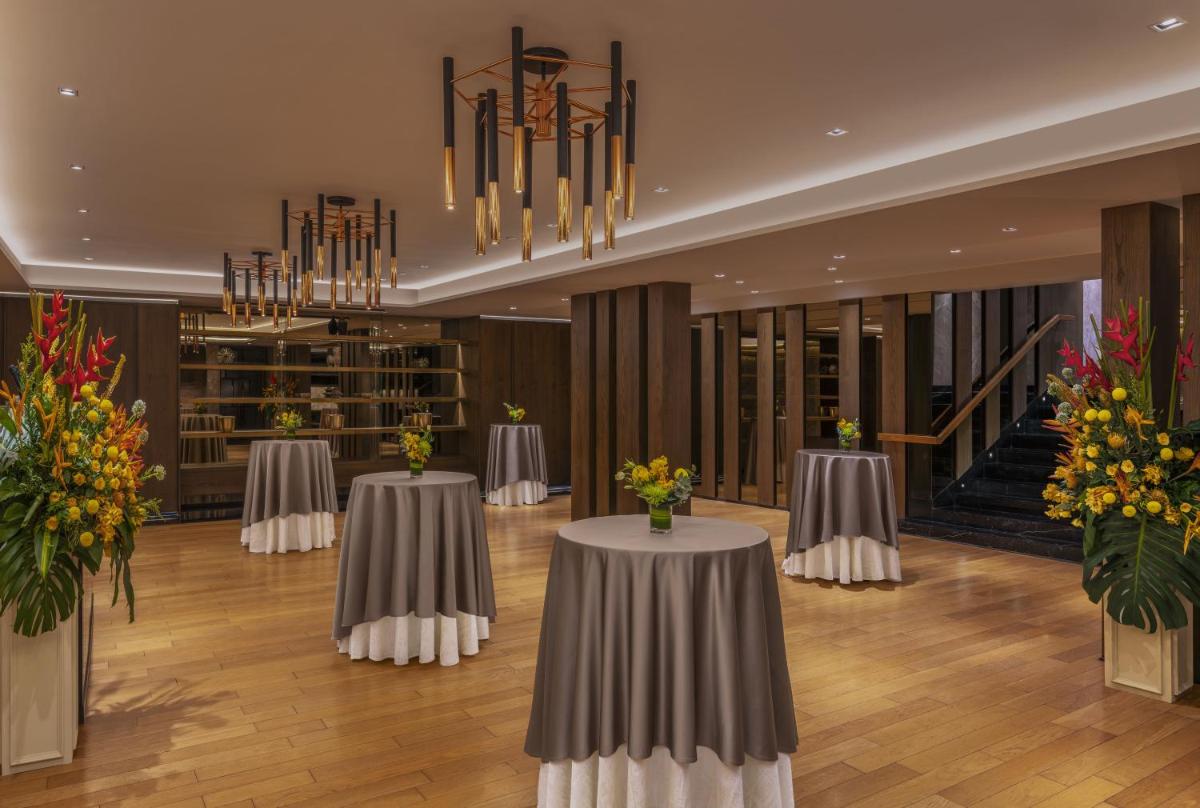 a banquet hall with two tables with flowers and a chandelier at The Raintree, St. Mary’s Road in Chennai