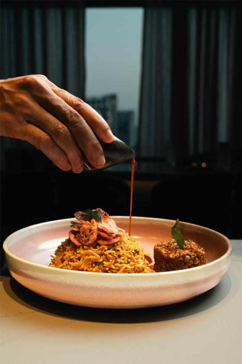 a person is sprinkling sauce on a plate of food at Radisson Blu Hotel Pune Kharadi in Pune