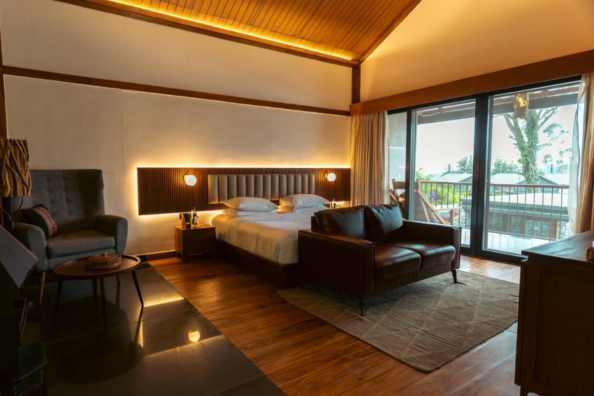 a bedroom with a bed and a couch and a chair at WelcomHeritage Ayatana Ooty in Ooty