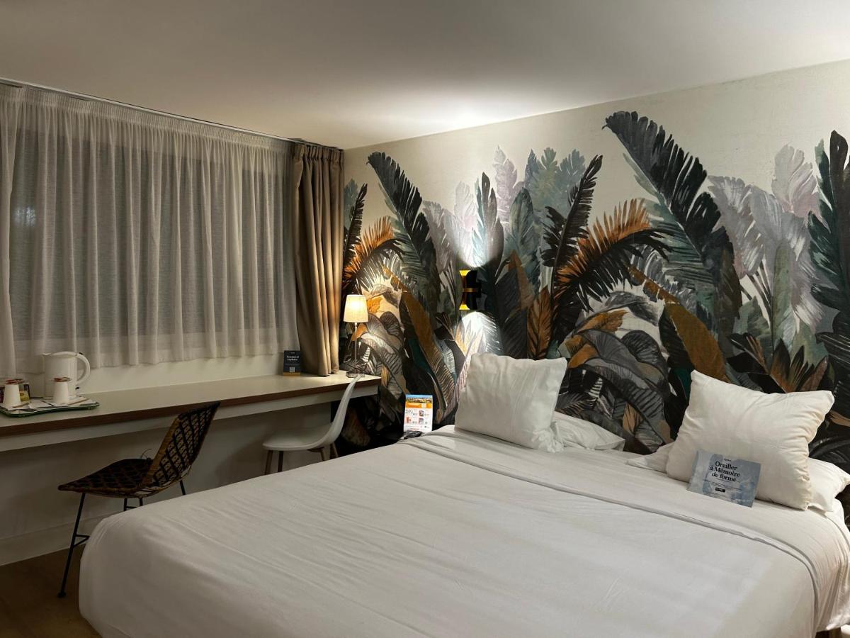 une chambre avec un grand lit blanc et un papier peint tropical dans l'établissement Kyriad Carcassonne - Aéroport, à Carcassonne