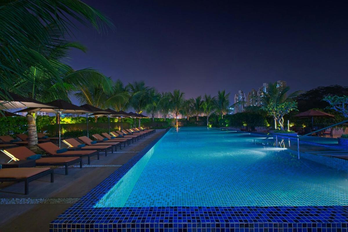 a swimming pool with chairs and palm trees at night at The Westin Mumbai Garden City in Mumbai