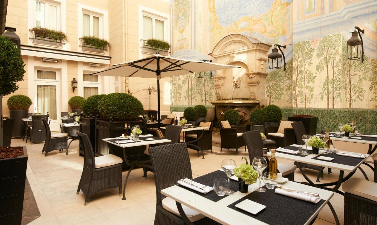 un restaurant avec des tables, des chaises et un parasol dans l'établissement Castille Paris – Starhotels Collezione, à Paris