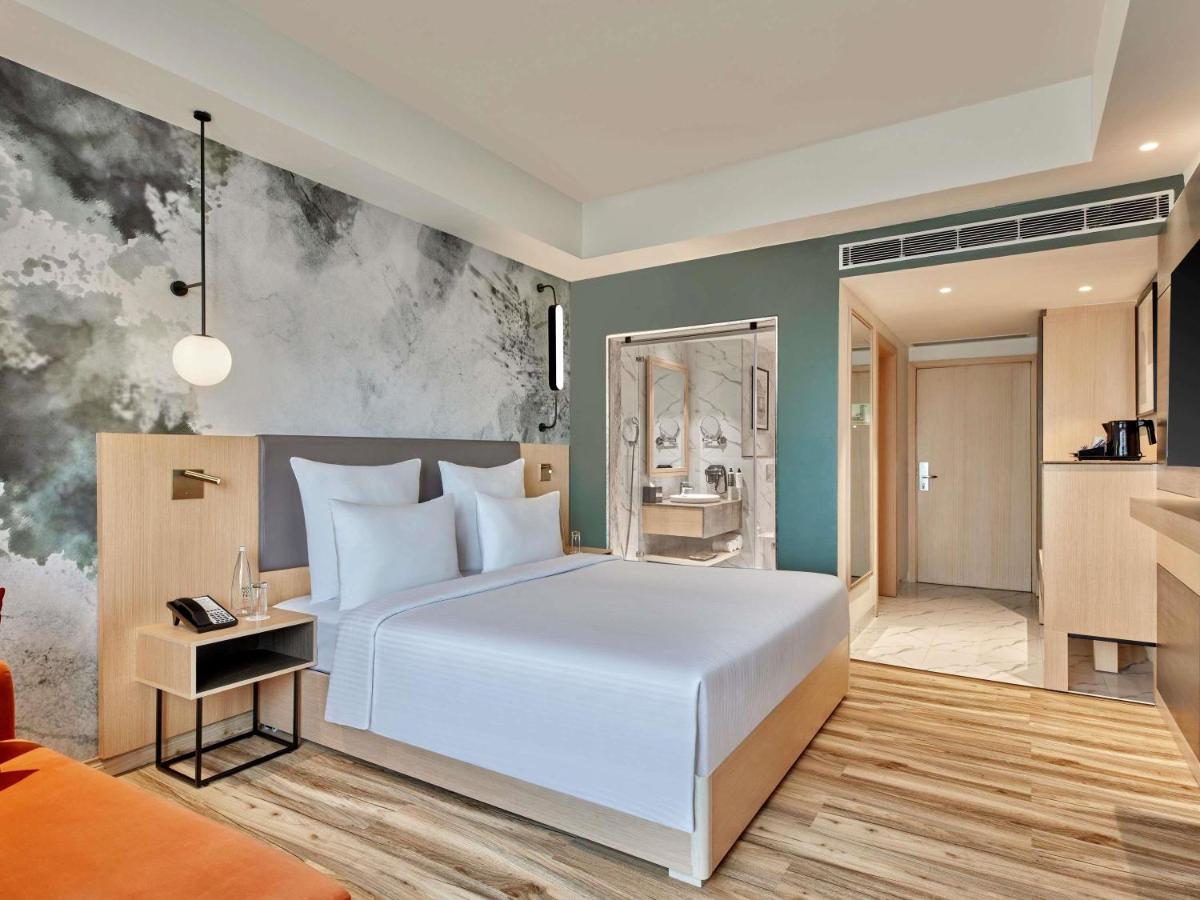 a bedroom with a large white bed and a kitchen at Novotel Jaipur Convention Centre in Jaipur