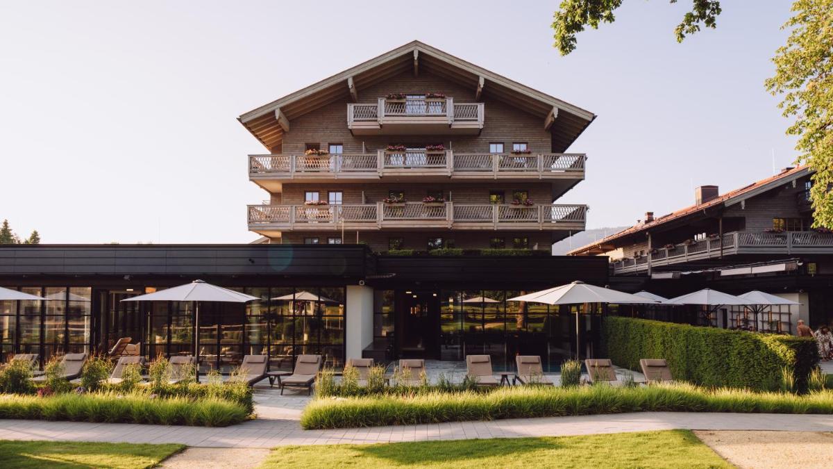 ein Gebäude mit Stühlen und Sonnenschirmen davor in der Unterkunft Parkhotel Egerner Höfe in Rottach-Egern