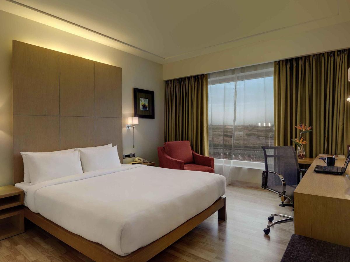 a hotel room with a bed and a desk and a window at Novotel Hyderabad Airport in Hyderabad