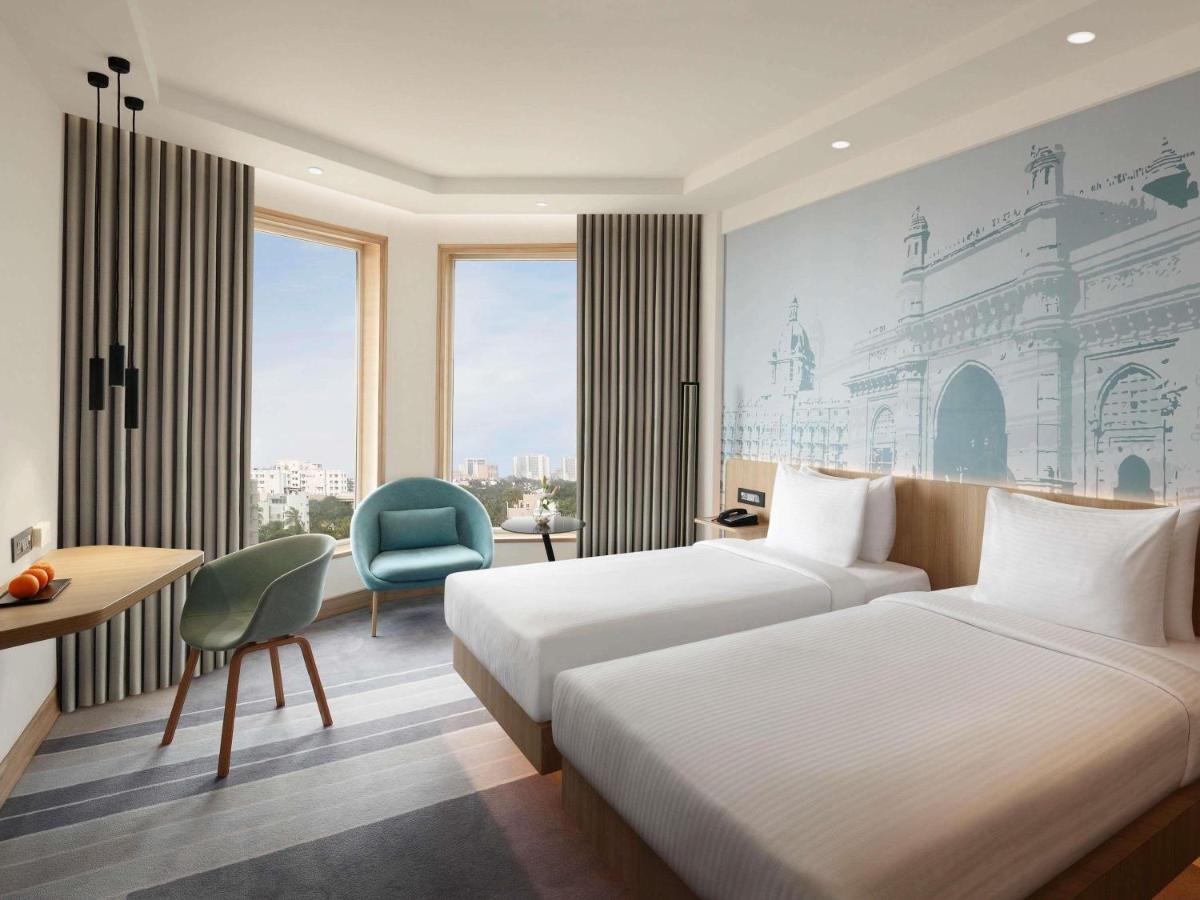 a hotel room with two beds and a desk and a chair at Novotel Mumbai Juhu Beach in Mumbai