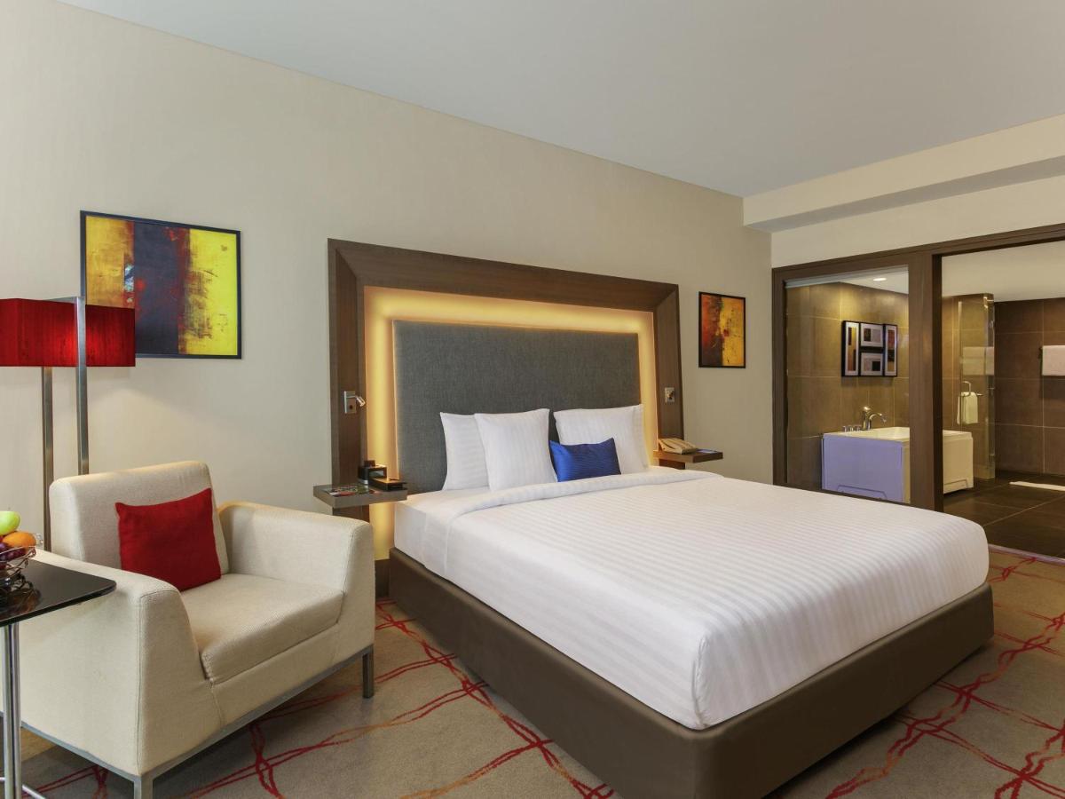 a bedroom with a large bed and a chair at Novotel Ahmedabad in Ahmedabad