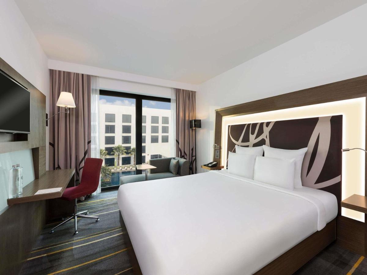 a hotel room with a large bed and a desk at Novotel New Delhi Aerocity in New Delhi a hotel room with a large bed and a desk at Novotel New Delhi Aerocity in New Delhi