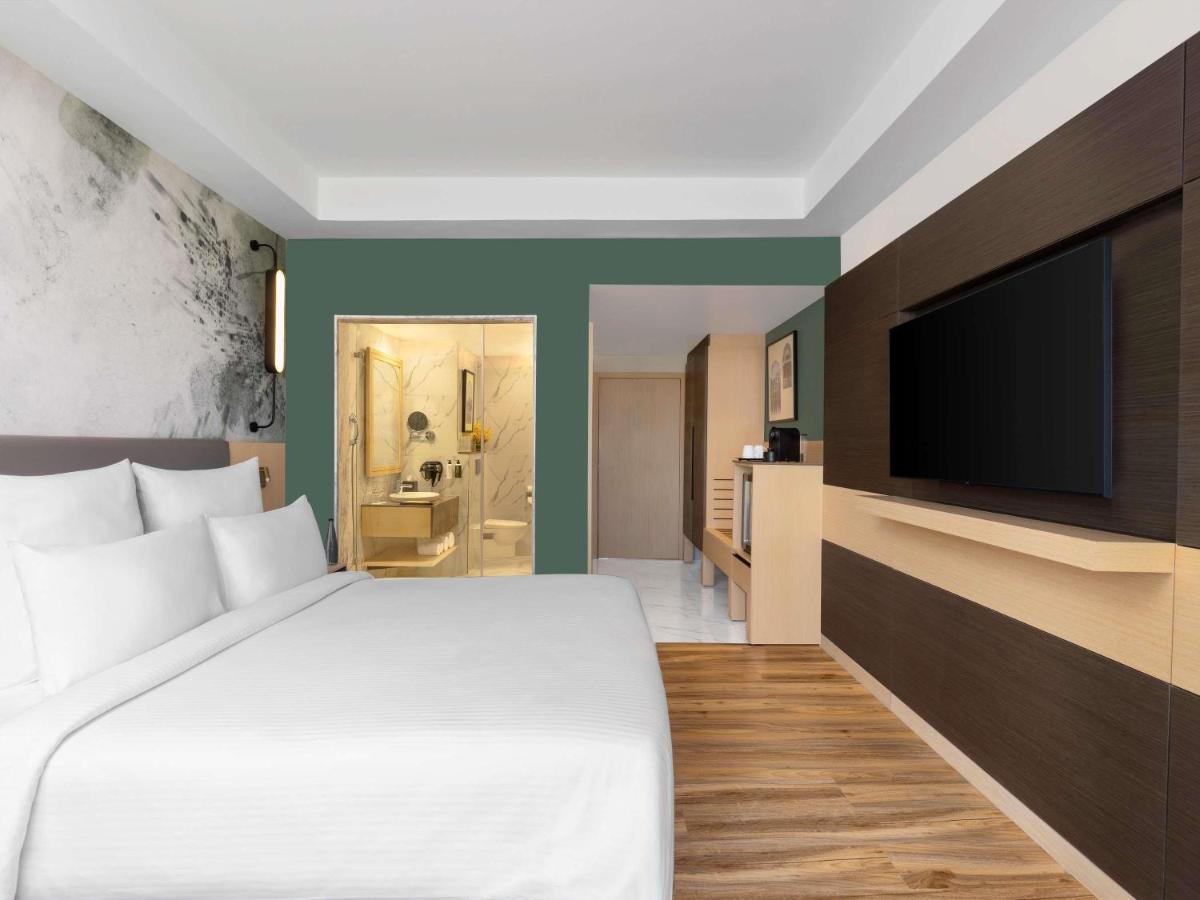 a bedroom with a large bed and a flat screen tv at Novotel Jaipur Convention Centre in Jaipur