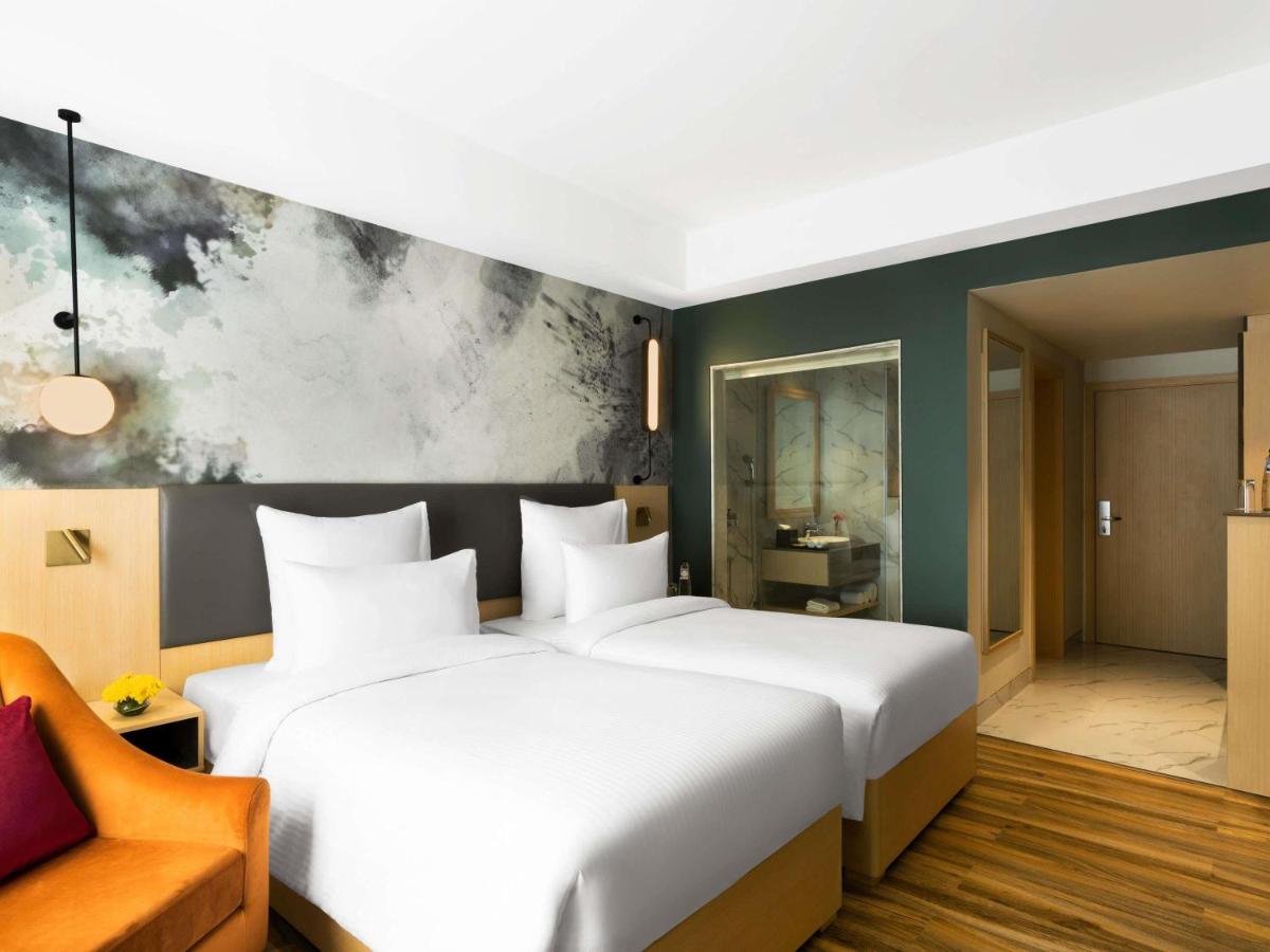 a bedroom with a large white bed and a chair at Novotel Jaipur Convention Centre in Jaipur