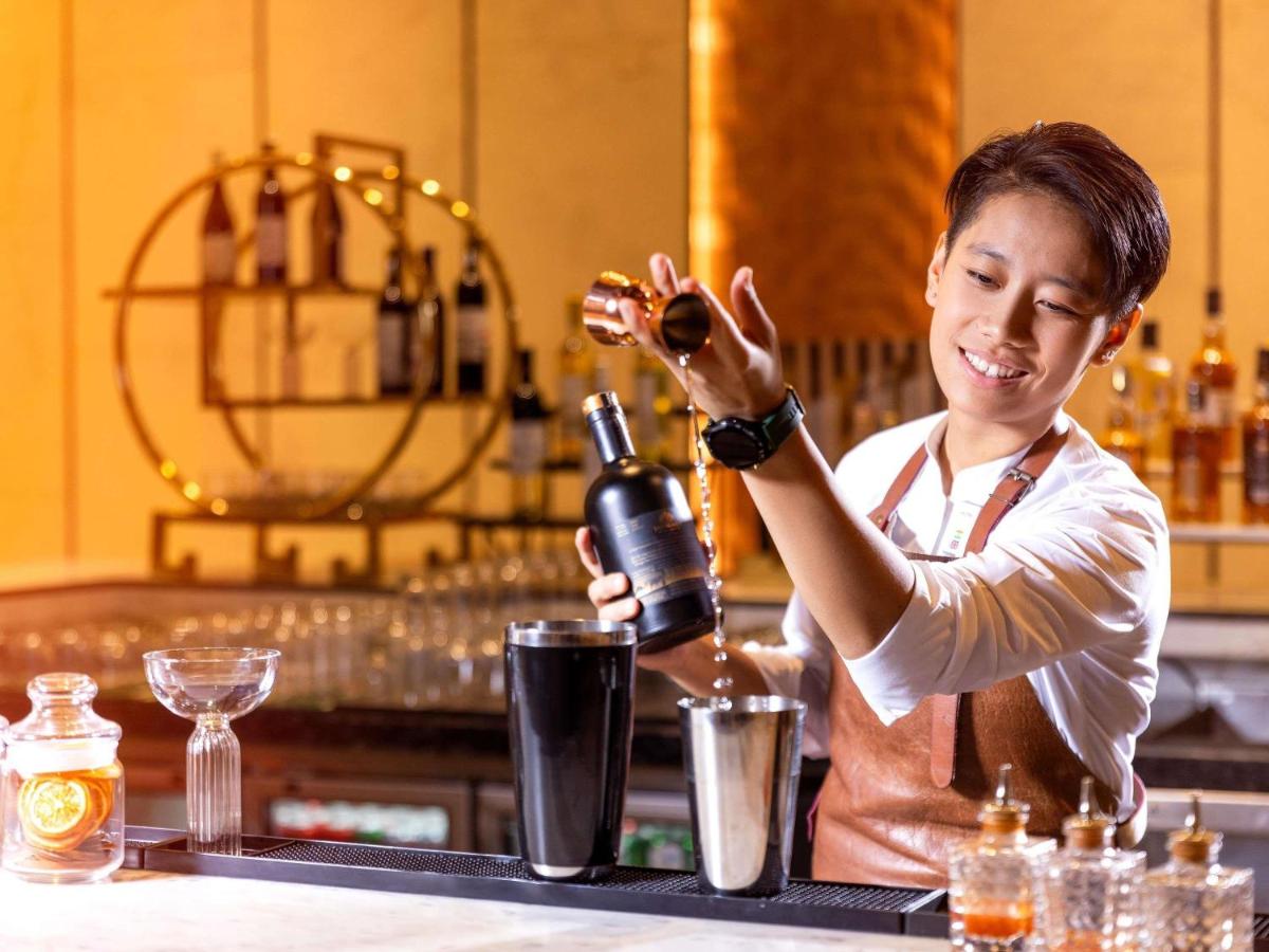 a woman standing at a bar pouring a bottle of wine at Novotel Jaipur Convention Centre in Jaipur