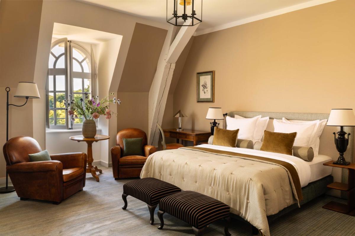 une chambre avec un grand lit et deux chaises dans l'établissement Château d'Augerville Golf & Spa Resort - TemptingPlaces Collection, à Augerville-la-Rivière 31 autres photos
