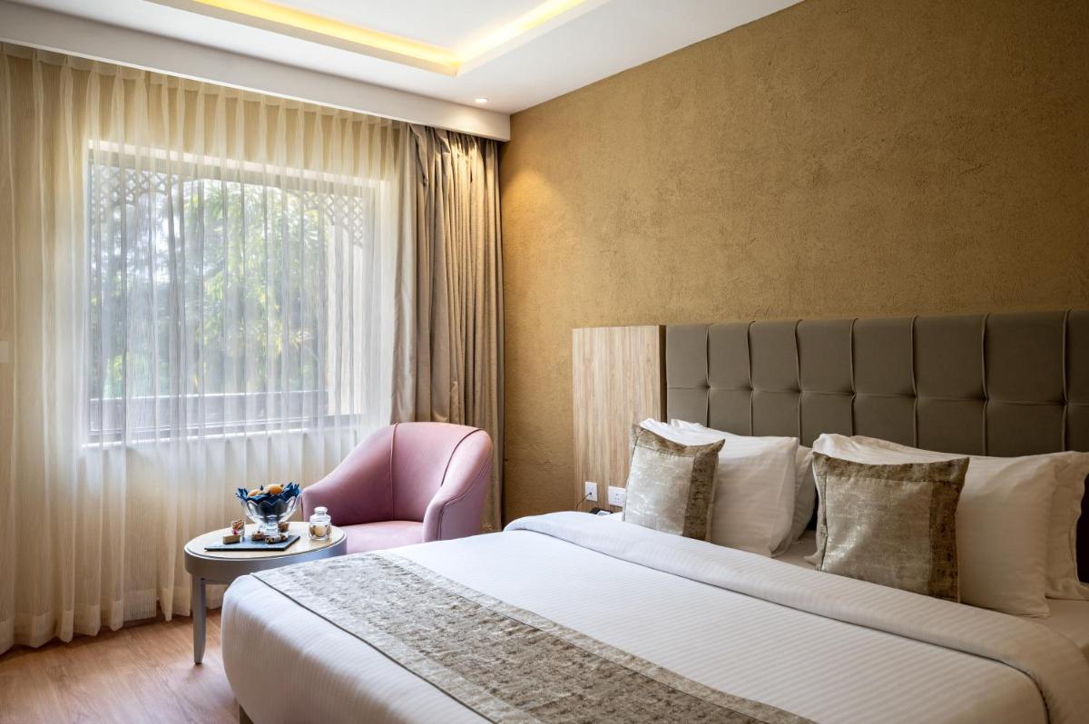 a bedroom with a large bed and a pink chair at Essentia Luxury Resort & Spa Udaipur in Udaipur