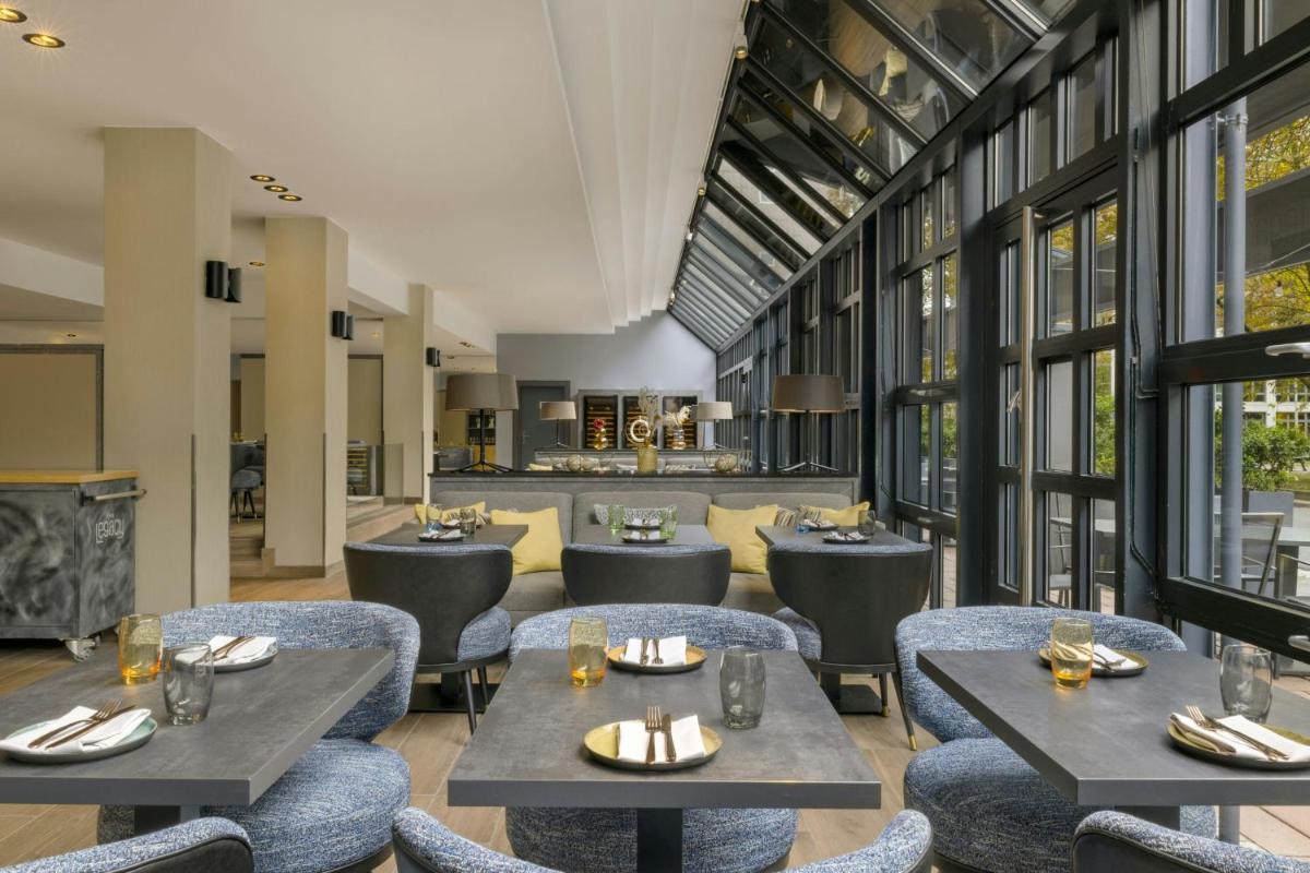 ein Restaurant mit Tischen, Stühlen und Fenstern in der Unterkunft Le Méridien Frankfurt in Frankfurt am Main