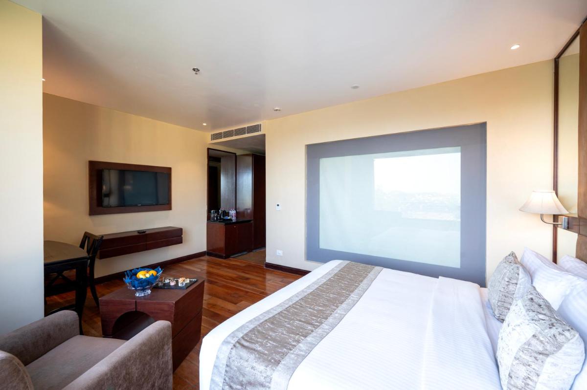 a large screen in a bedroom with a bed and a couch at Essentia Luxury Resort & Spa Udaipur in Udaipur