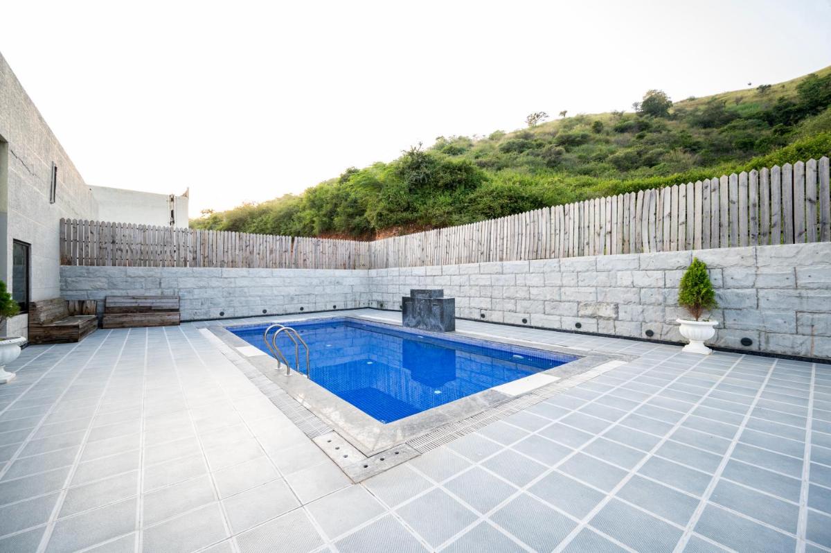 a swimming pool in a backyard with a stone wall at Essentia Luxury Resort & Spa Udaipur in Udaipur