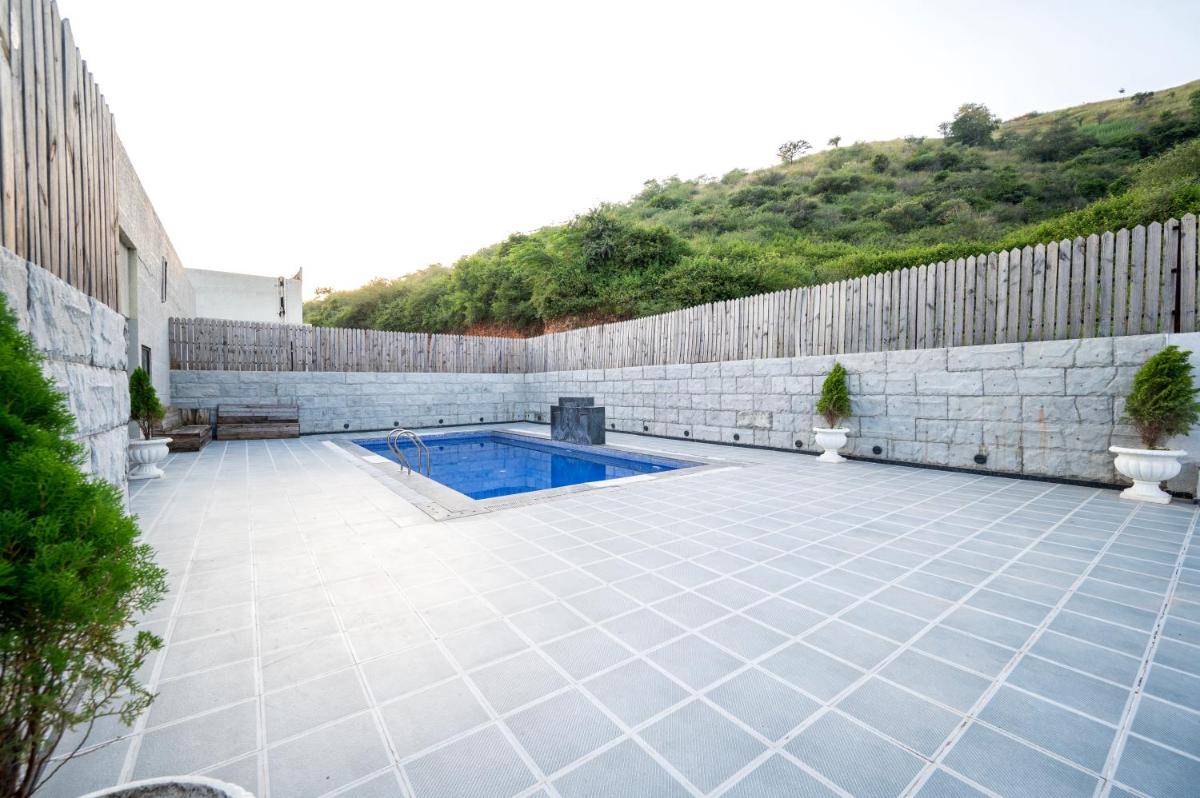 a swimming pool on a tiled patio with a stone wall at Essentia Luxury Resort & Spa Udaipur in Udaipur