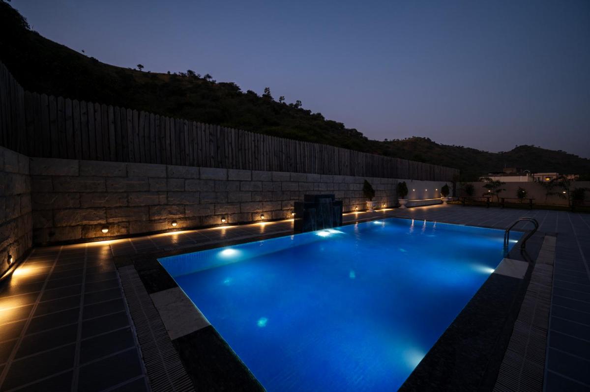 a swimming pool lit up at night with lights at Essentia Luxury Resort & Spa Udaipur in Udaipur