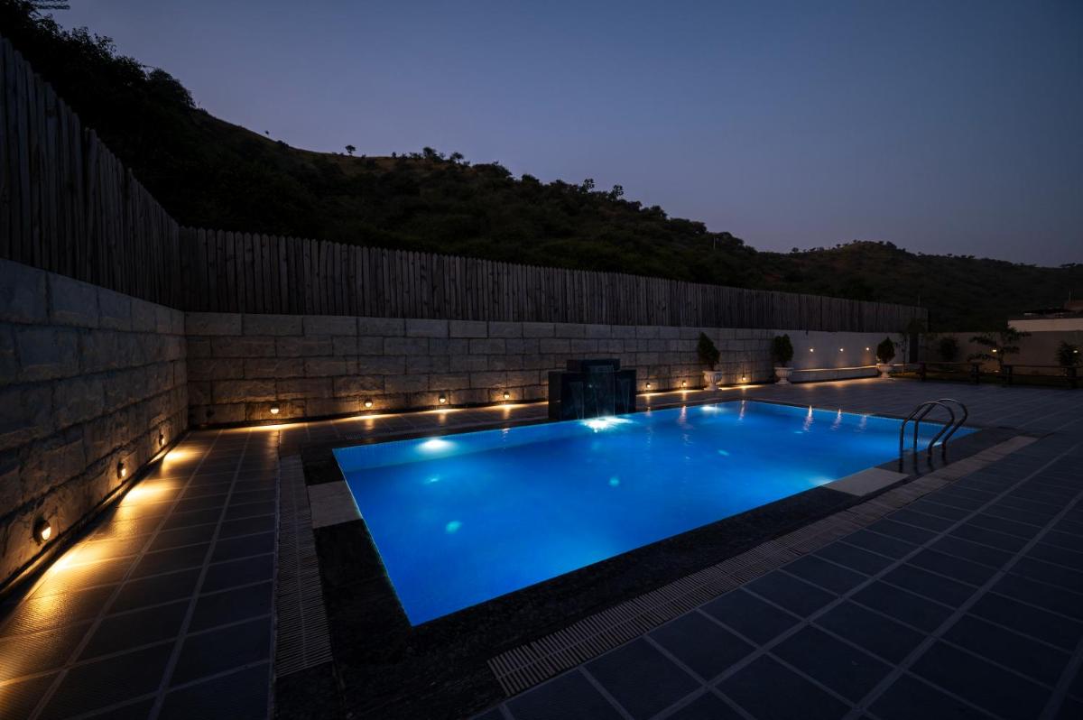 a swimming pool lit up at night with lights at Essentia Luxury Resort & Spa Udaipur in Udaipur