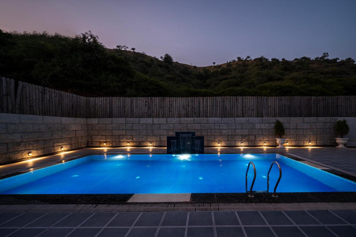 a swimming pool lit up at night with lights at Essentia Luxury Resort & Spa Udaipur in Udaipur