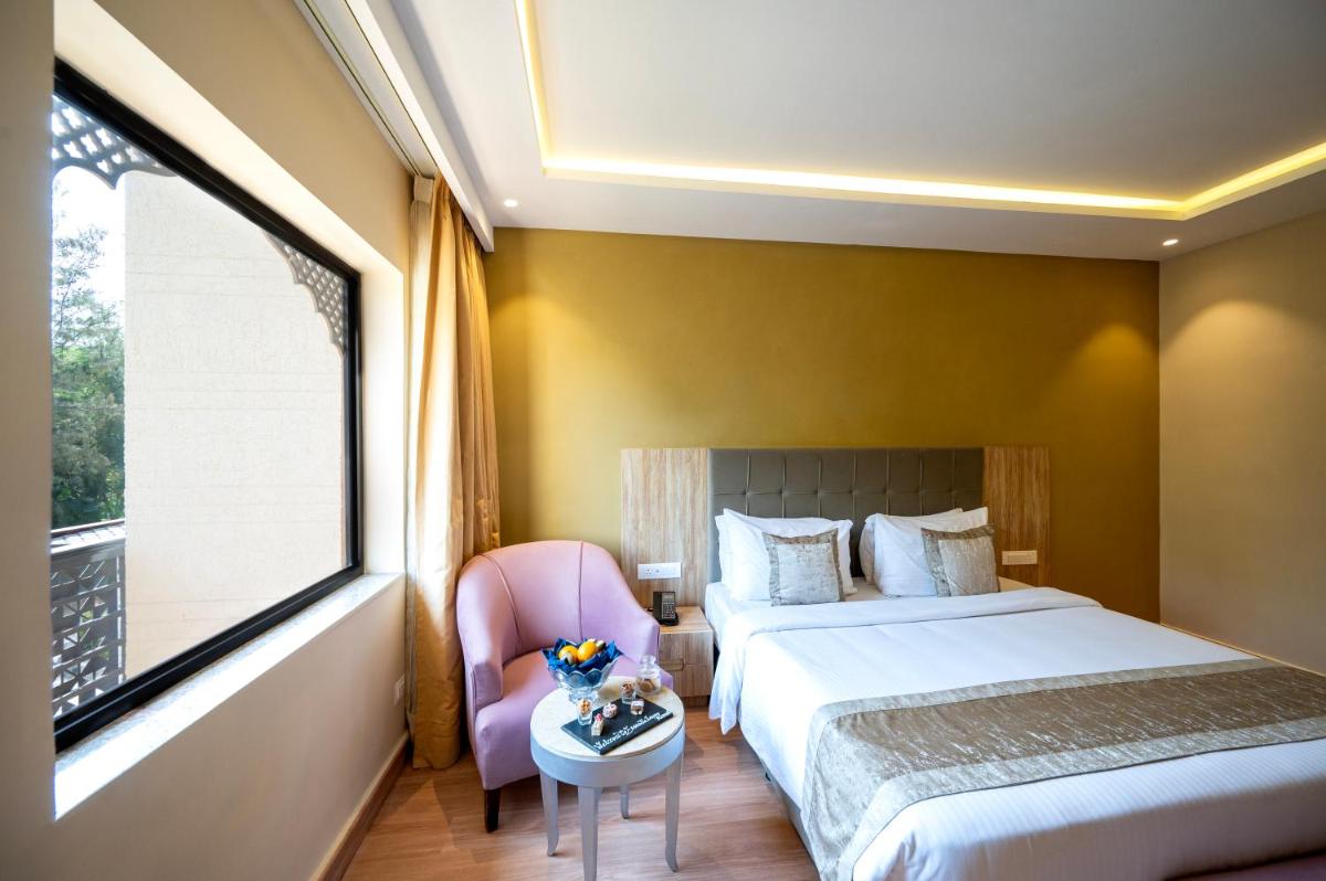 a bedroom with a bed and a chair and a window at Essentia Luxury Resort & Spa Udaipur in Udaipur