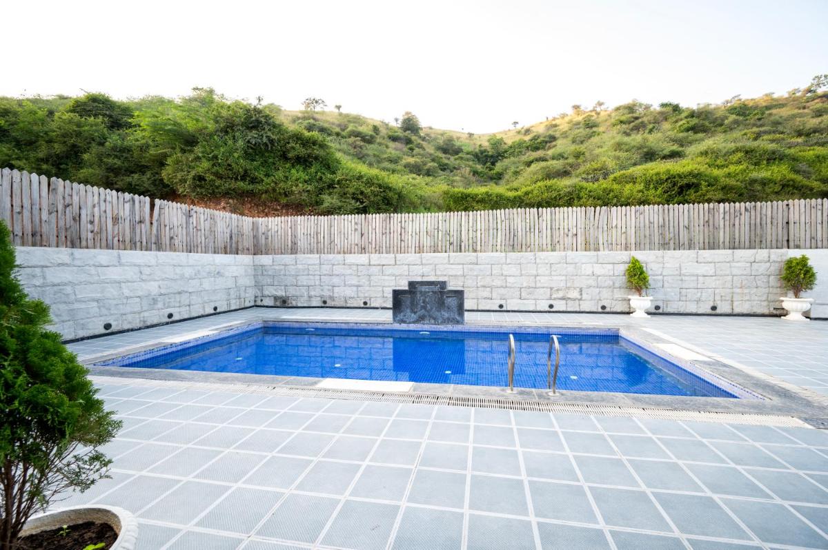 a swimming pool in a yard next to a wooden fence at Essentia Luxury Resort & Spa Udaipur in Udaipur