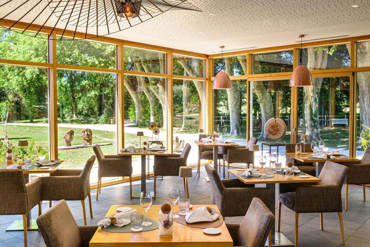 un restaurant avec des tables et des chaises et de grandes fenêtres dans l'établissement Château De Massillan, à Uchaux