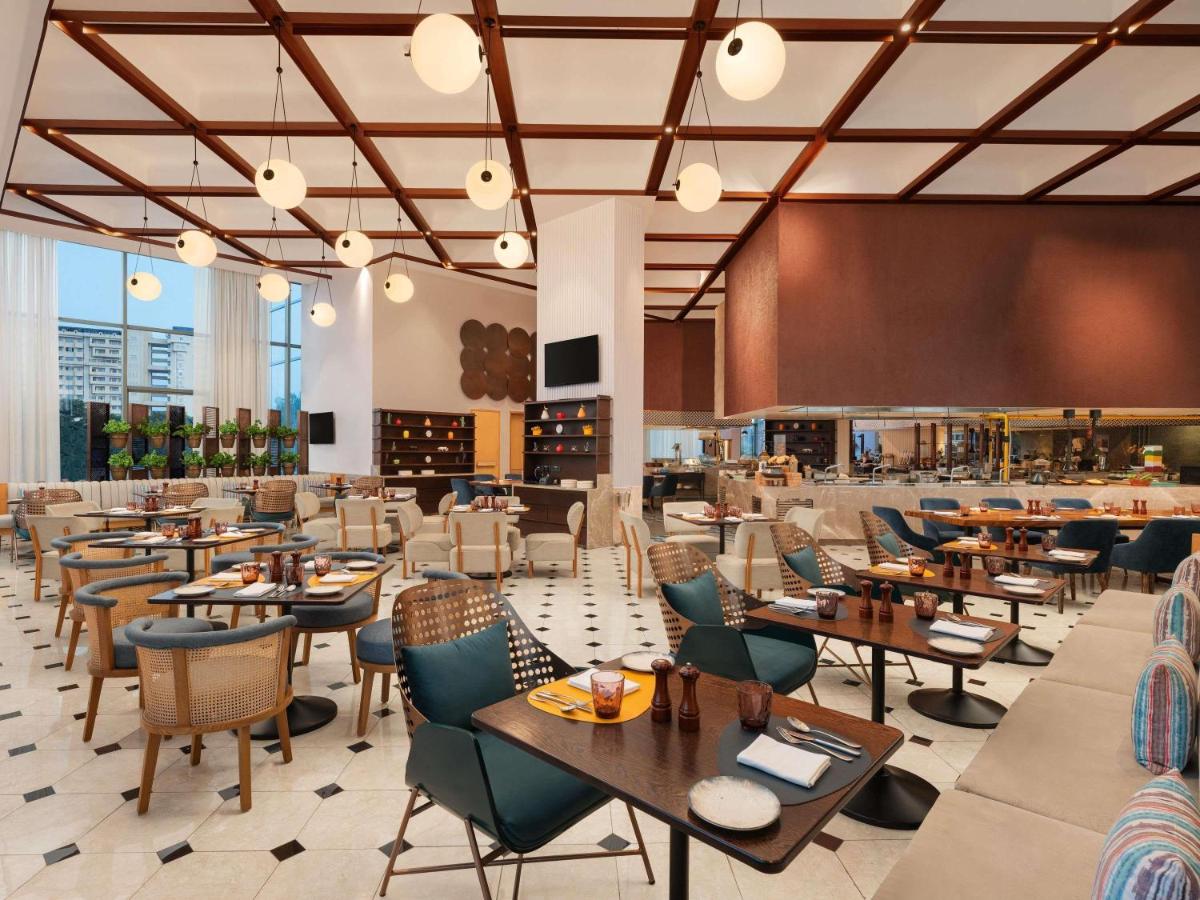 Un restaurante con mesas y sillas y un bar. en Novotel New Delhi City Centre, en Nueva Delhi Un restaurante con mesas y sillas y un bar. en Novotel New Delhi City Centre, en Nueva Delhi