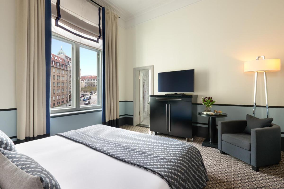 ein Hotelzimmer mit Bett, Fernseher und Stuhl in der Unterkunft Hotel De Rome Berlin in Berlin