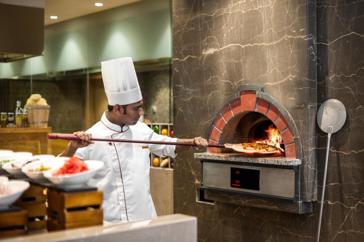 a chef taking a pizza out of an oven at Feathers- A Radha Hotel, Chennai in Chennai