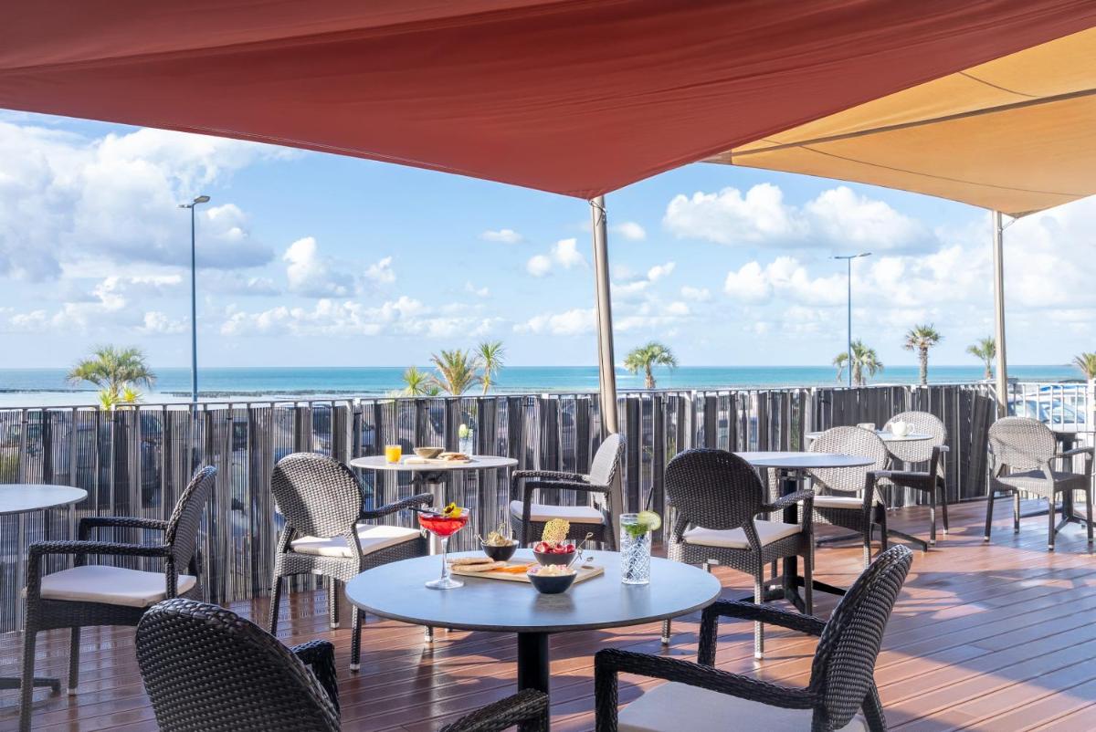 une terrasse avec des tables et des chaises et l'océan dans l'établissement Hôtel de la Baie - Thalassothérapie PREVITHAL, à Donville-les-Bains