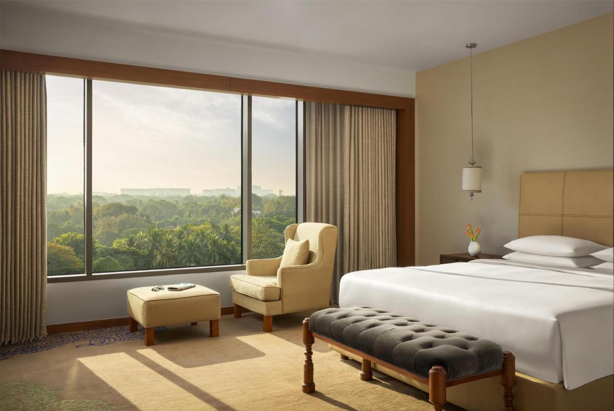a bedroom with a bed and a chair and a large window at Park Hyatt Chennai in Chennai