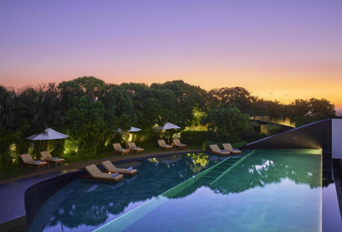 a swimming pool with chairs and umbrellas at sunset at Park Hyatt Chennai in Chennai