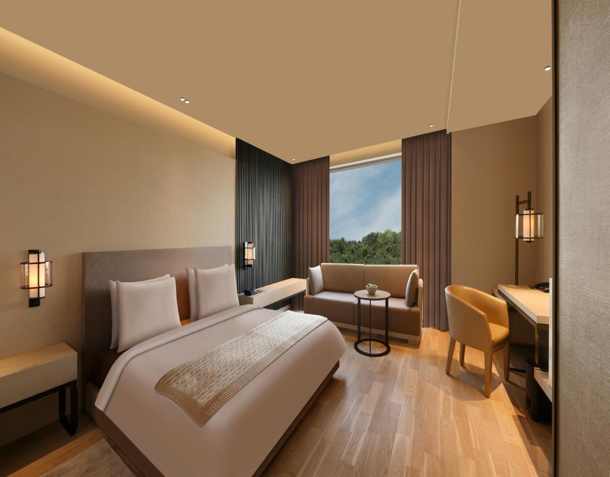 a hotel room with a bed and a desk and a chair at Roseate House New Delhi in New Delhi a hotel room with a bed and a desk and a chair at Roseate House New Delhi in New Delhi