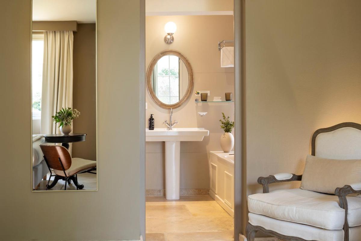 une salle de bains avec un miroir, un lavabo et une chaise dans l'établissement Château Les Oliviers de Salettes, à Charols