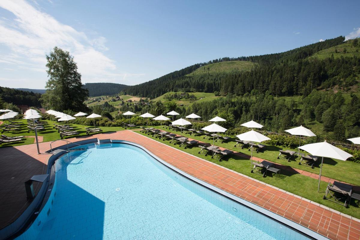 einen Pool mit Sonnenschirmen, Tischen und Stühlen in der Unterkunft Hotel Traube Tonbach in Baiersbronn