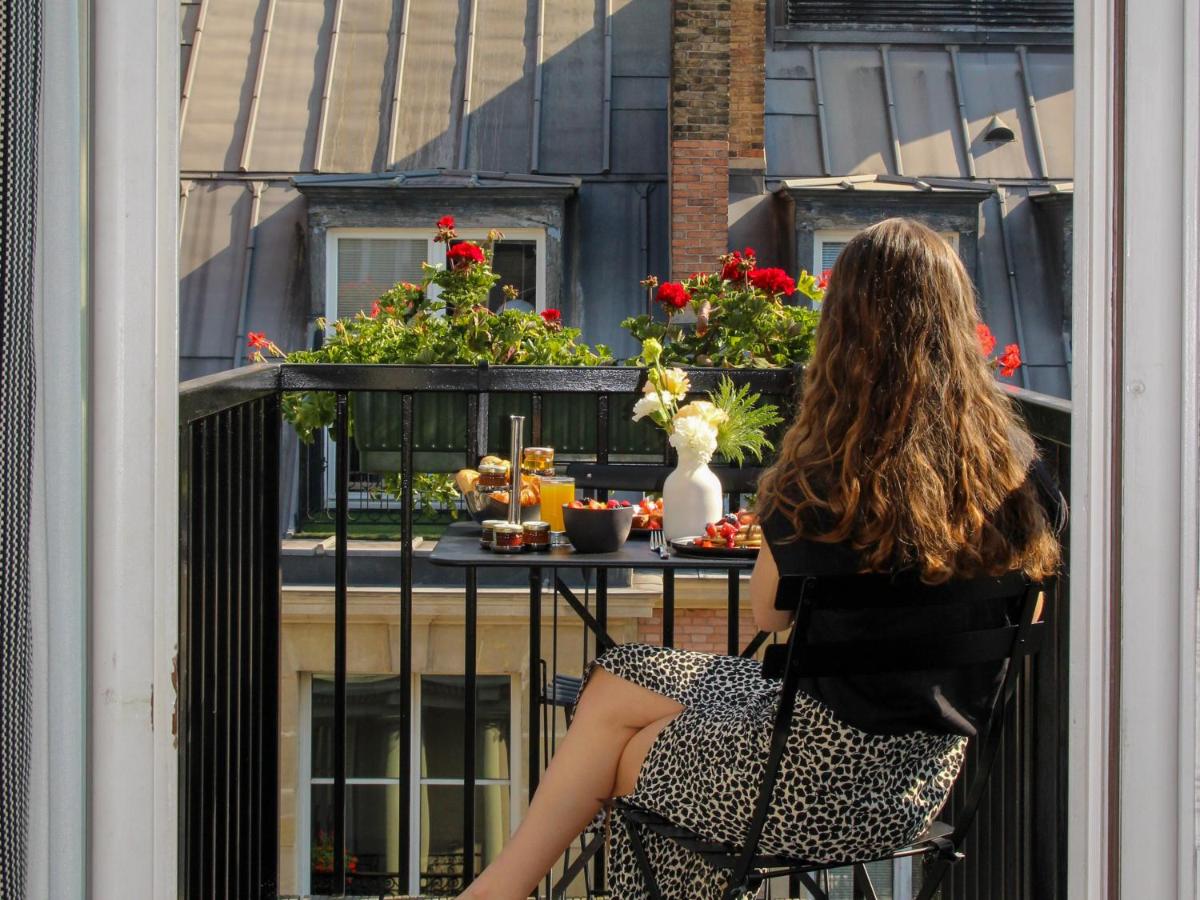 une femme assise sur une chaise sur un balcon regardant par une fenêtre dans l'établissement Hôtel Vernet Champs Elysées Paris, à Paris
