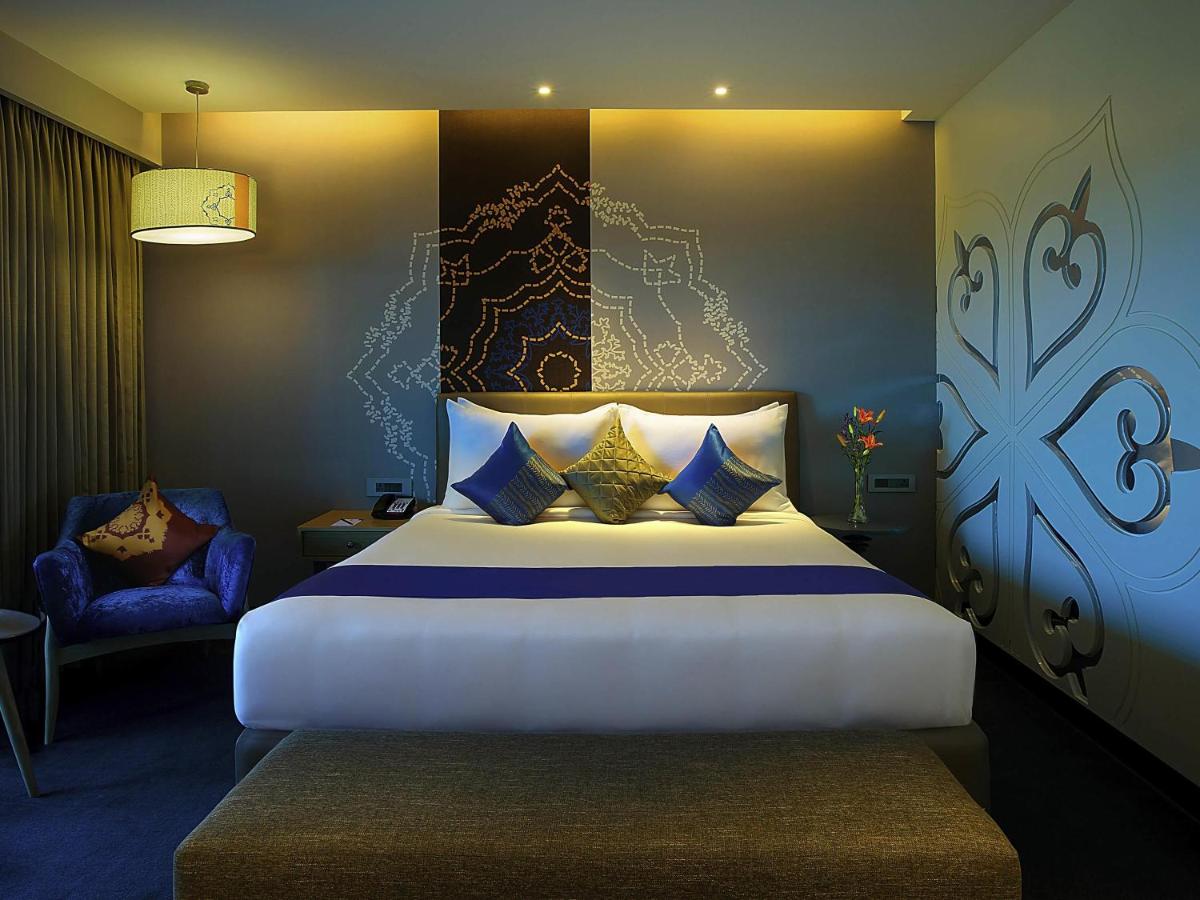 a bedroom with a large bed and a chair at Grand Mercure Mysore - An Accor Brand in Mysore