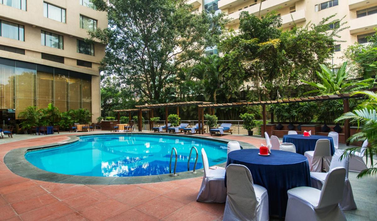 a pool with tables and chairs next to a building at The Chancery Pavilion in Bengaluru