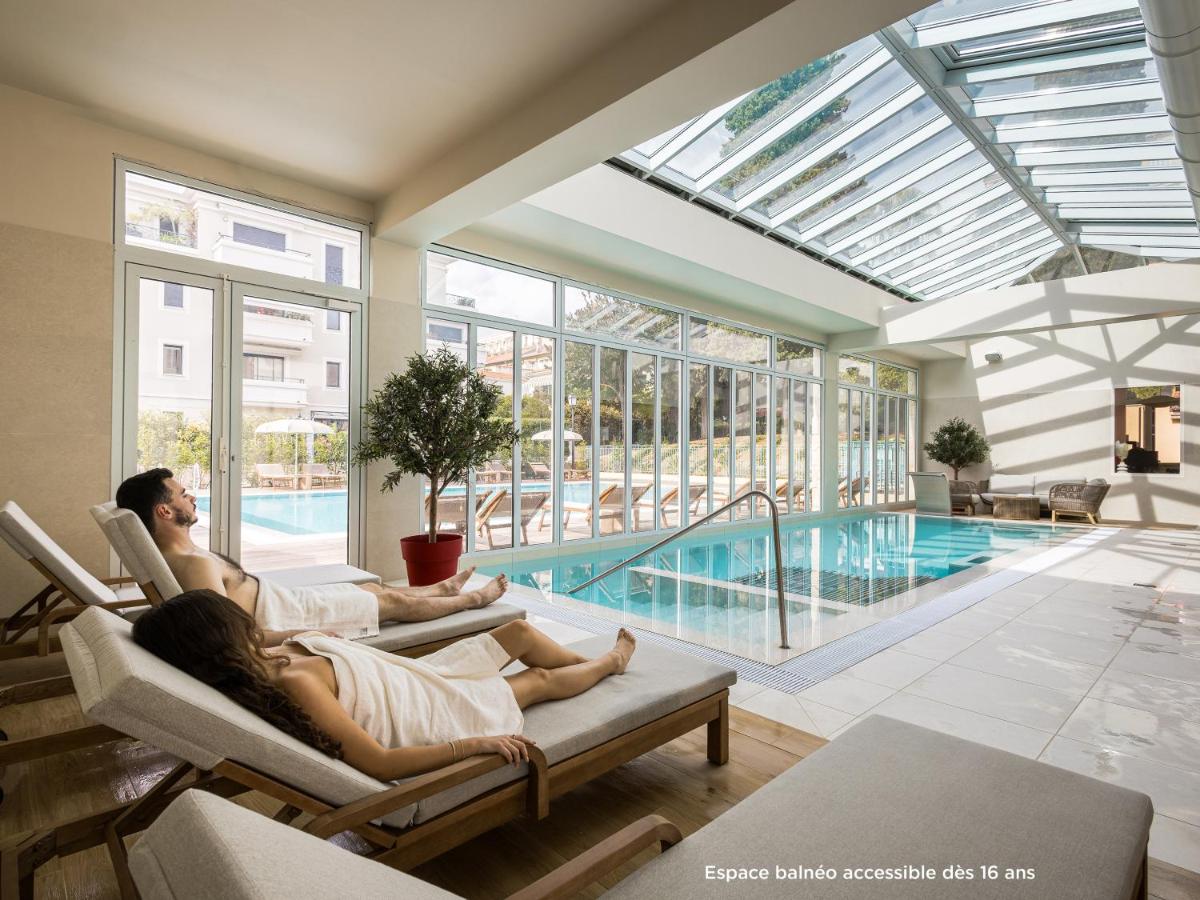deux personnes assises sur des chaises dans un salon avec piscine dans l'établissement Hôtel Miléade L'Orangeraie - entièrement rénové, à Menton